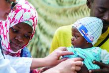 A white doctor with a stethoscope examines an African baby, while the parents look on.